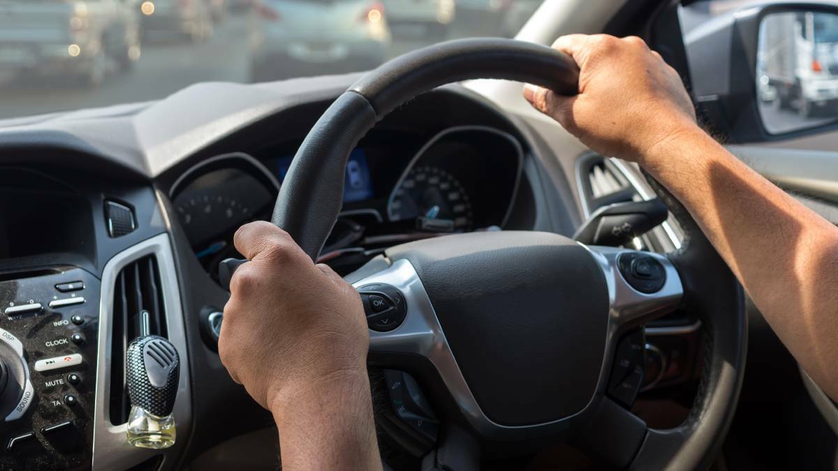 A person with their hands on a car's steering wheel. File picture
