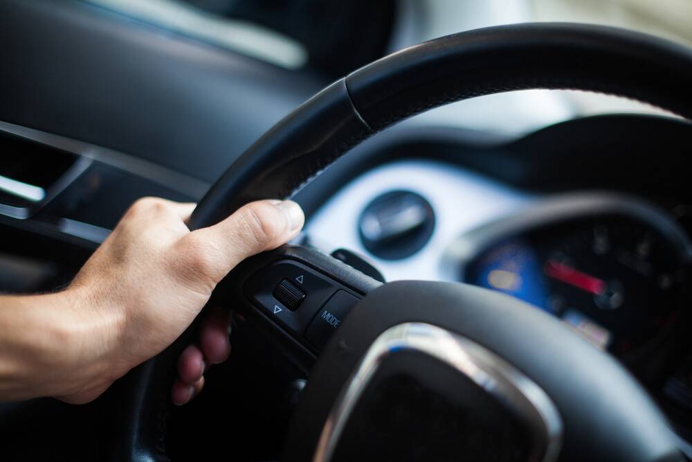 A person with their left hand on the steering wheel of a vehicle. File picture