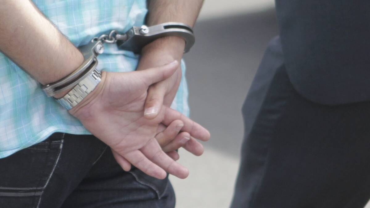 A person with their hands behind their back in handcuffs being escorted by an officer of the court. File picture